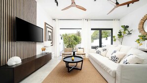 Ein modernes Wohnzimmer mit Flachbildfernseher, einer Couch, einem Couchtisch und einem Deckenventilator.
