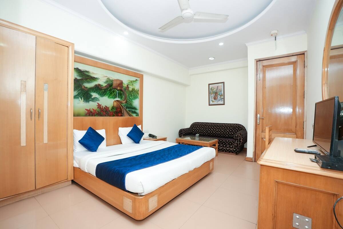 Una habitación de hotel con cama, sofá, escritorio y televisor, además de un ventilador de techo.