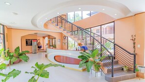 A spacious lobby with a curved reception desk, a staircase with metal railings, and potted plants. - Dinah's Tourist Inn Puerto Princesa (Puerto Princesa)