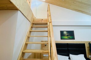 A wooden ladder leading to a loft bedroom with a black headboard and a painting of a landscape. - Manali Vibes (Manali)