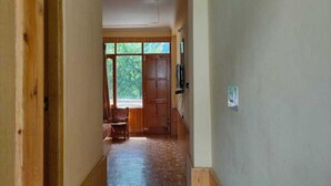 A hallway with wooden flooring, a wooden door at the end, and a window with a view of greenery. - Antriksh Cottage Manali (Manali)