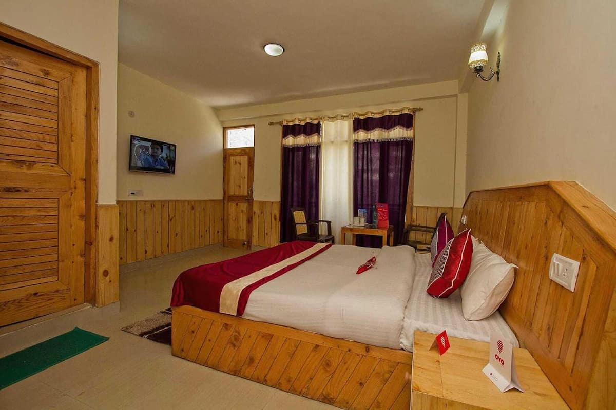 A room with a wooden bed, a small table, a chair, and a television on the wall.