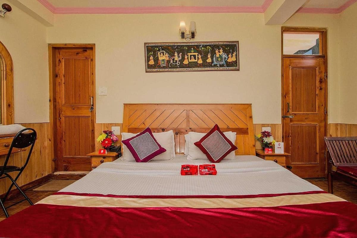 A bedroom with a wooden headboard, two nightstands with lamps, a bed with a red blanket, and a wall-mounted painting.