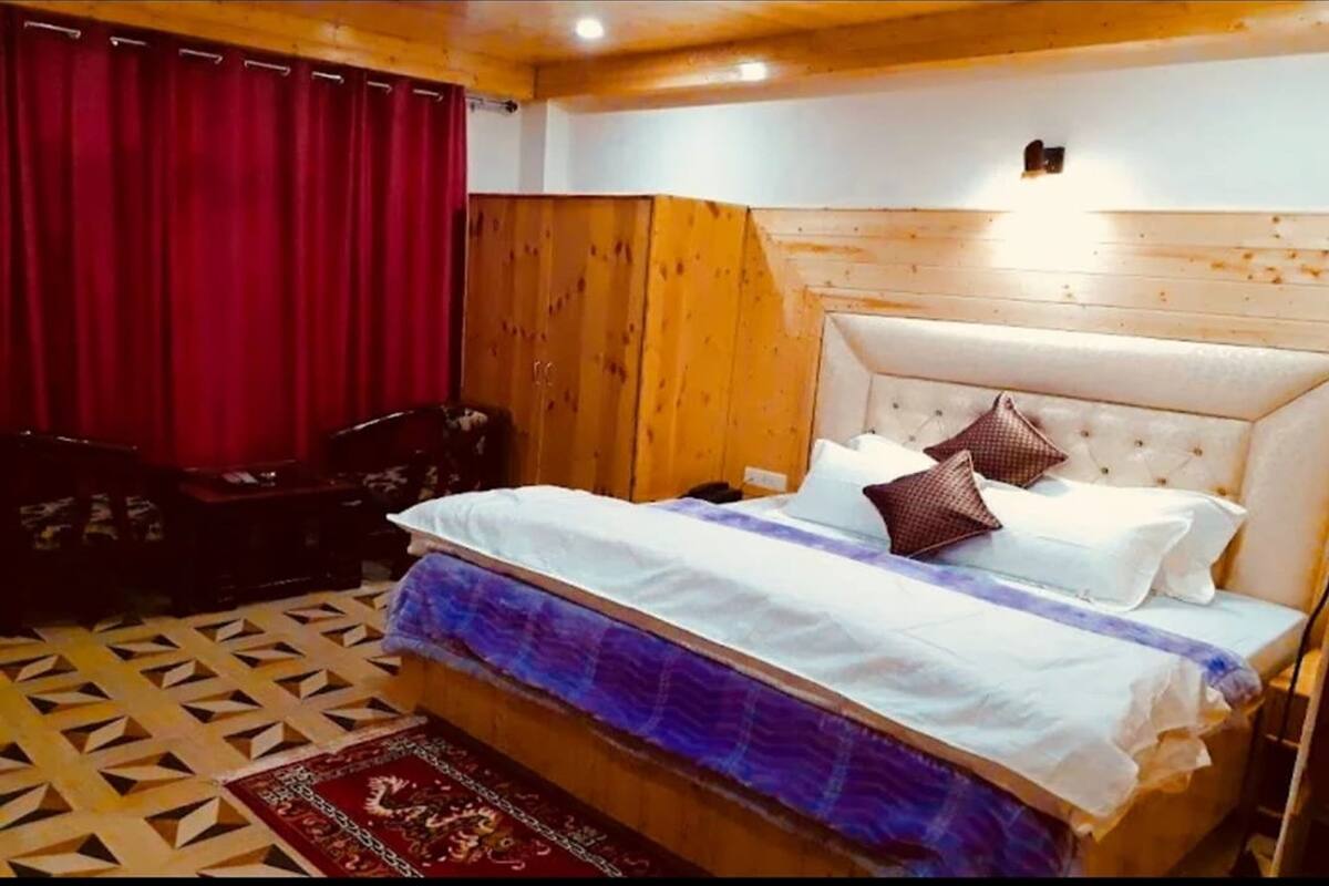 A bedroom with a bed, wooden headboard, red curtains, and patterned carpet.