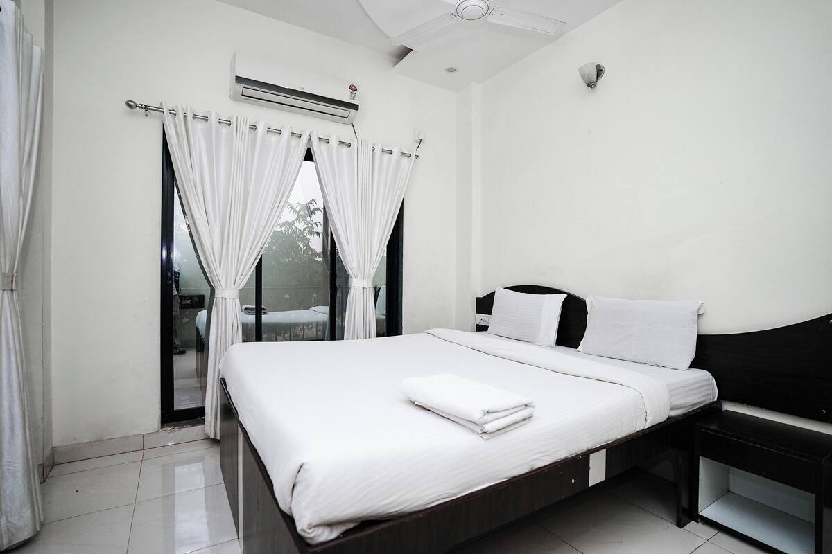 A modern hotel room with a large bed, a bedside table, and a window with curtains.