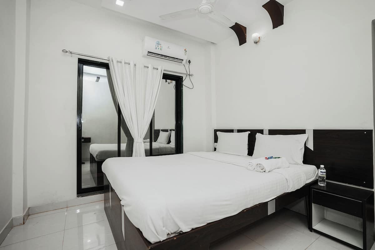 A hotel room with a large bed, a bedside table, a ceiling fan, and an air conditioning unit.
