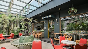 A cafe with indoor seating, a central planter, and a view of the street through large windows. - Bangreng Inn (Bandung)