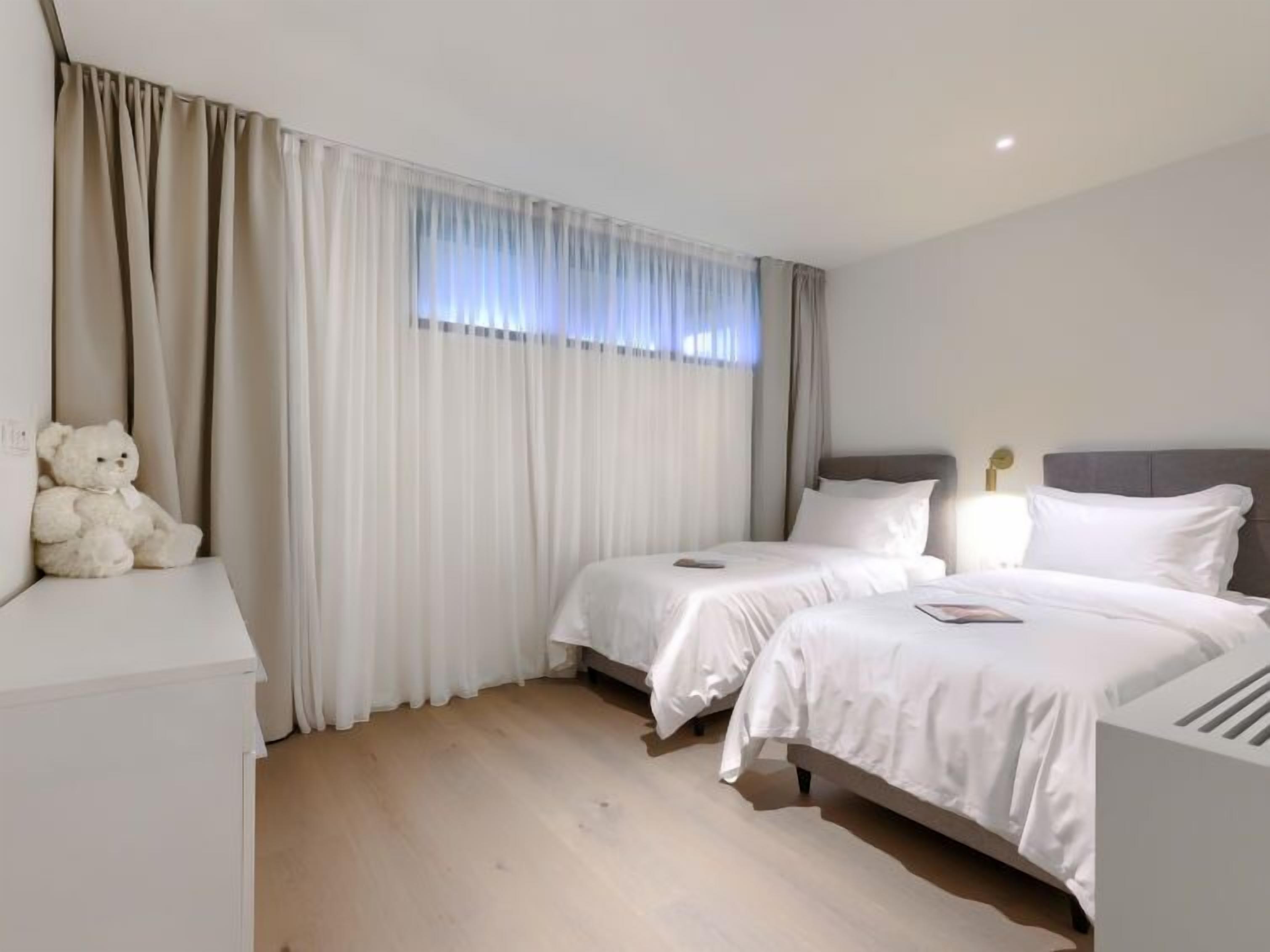 Une chambre d’hôtel avec deux lits, une commode blanche et un ours en peluche.