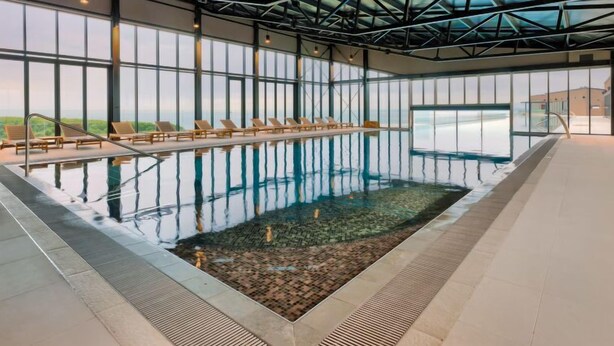An indoor swimming pool with clear glass walls, lounge chairs, and a view of the landscape. - Semi-detached Villa Crveni vrh 1.2.3. by Interhome (Umag/Savudrija)
