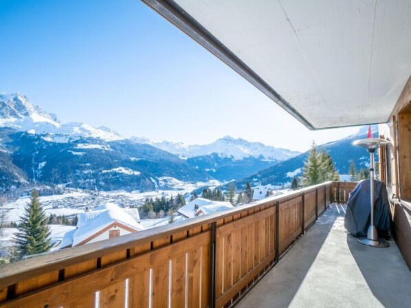 Ein Balkon mit Holzgeländer mit Blick auf eine verschneite Berglandschaft.