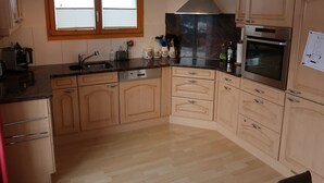 A kitchen with wooden cabinets, a stainless steel range hood, a built-in oven, and a window with blinds.
