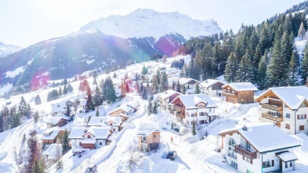 A snow-covered mountain village with wooden houses and a ski slope.