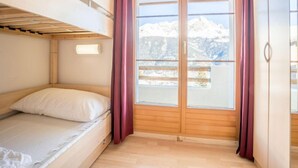 Een kamer met een stapelbed, een groot raam met gordijnen en uitzicht op besneeuwde bergen.