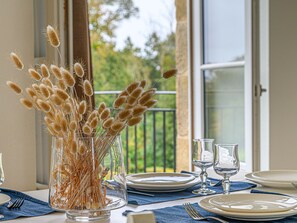 Un tavolo da pranzo con un vaso di vetro trasparente contenente piante essiccate, apparecchiato con piatti bianchi, posate e bicchieri da vino.