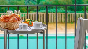 A table with croissants, orange slices, and coffee cups by a poolside with a wooden fence and greenery in the background. - Château De Kergonano by Interhome (Baden)