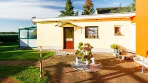 Una casa con un vialetto in mattoni che conduce a una porta in legno, immersa in un giardino con piante in vaso e un'antenna parabolica sul tetto.