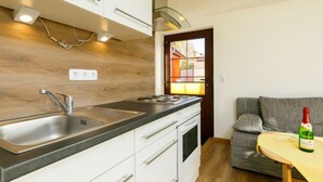 Una cucina moderna con mobili bianchi, lavello in acciaio inossidabile e piano di lavoro in legno. Si vede una finestra che offre vista su un edificio.