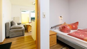 Una stanza compatta con un letto, un piccolo comodino in legno, una scrivania con una sedia e un divano.