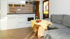 Una cucina compatta con mobili bianchi, forno integrato e un piccolo tavolo da pranzo con una bottiglia e della frutta.