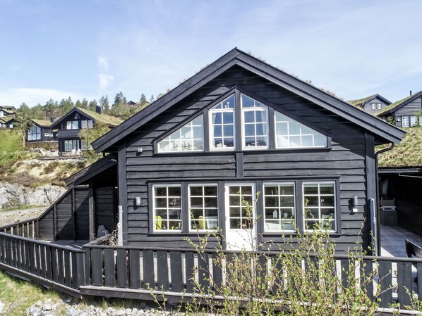 A two-story wooden cabin with large windows, a wooden deck, and a surrounding wooden fence.