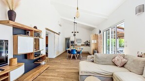 Ein modernes Wohnzimmer mit einer Couch, einem Couchtisch und einem Fernseher. Es gibt eine Küchenzeile mit einem Esstisch und Stühlen.