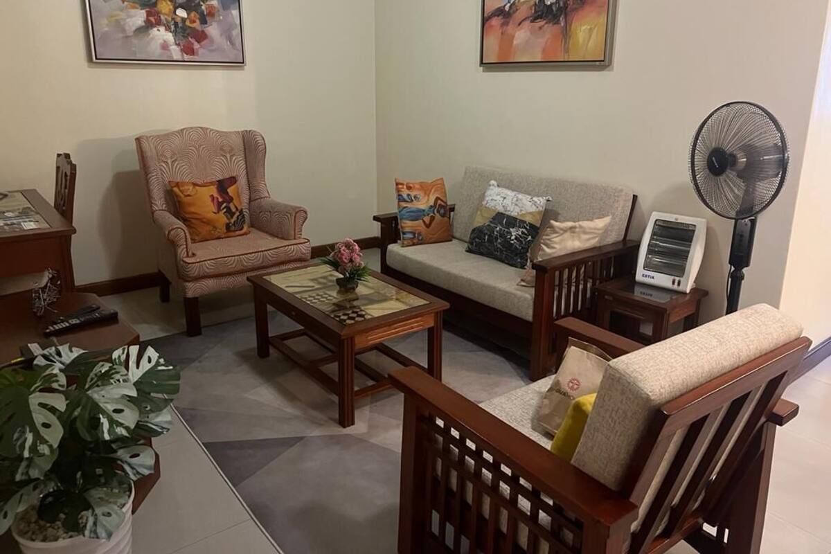 Een woonkamer met een bank, fauteuil, salontafel en een ventilator.