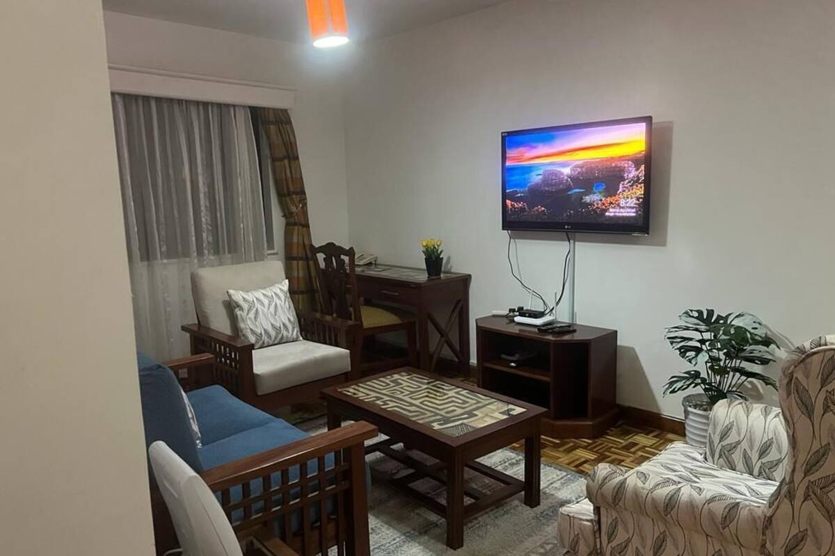 Een woonkamer met een bank, fauteuil, salontafel, televisie en een plant.