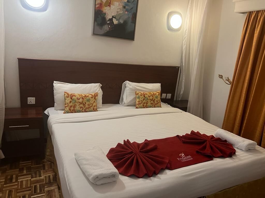 Une chambre d’hôtel avec un lit bien fait, une table de chevet, un tableau au mur et une fenêtre avec des rideaux.