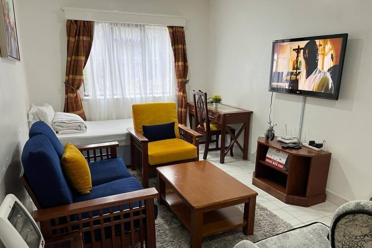 Een woonkamer met een bank, fauteuil, salontafel, televisie en een eettafeltje.
