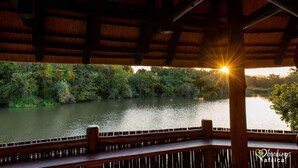 Eine Holzterrasse mit Blick auf einen Fluss, im Hintergrund ein Sonnenuntergang.