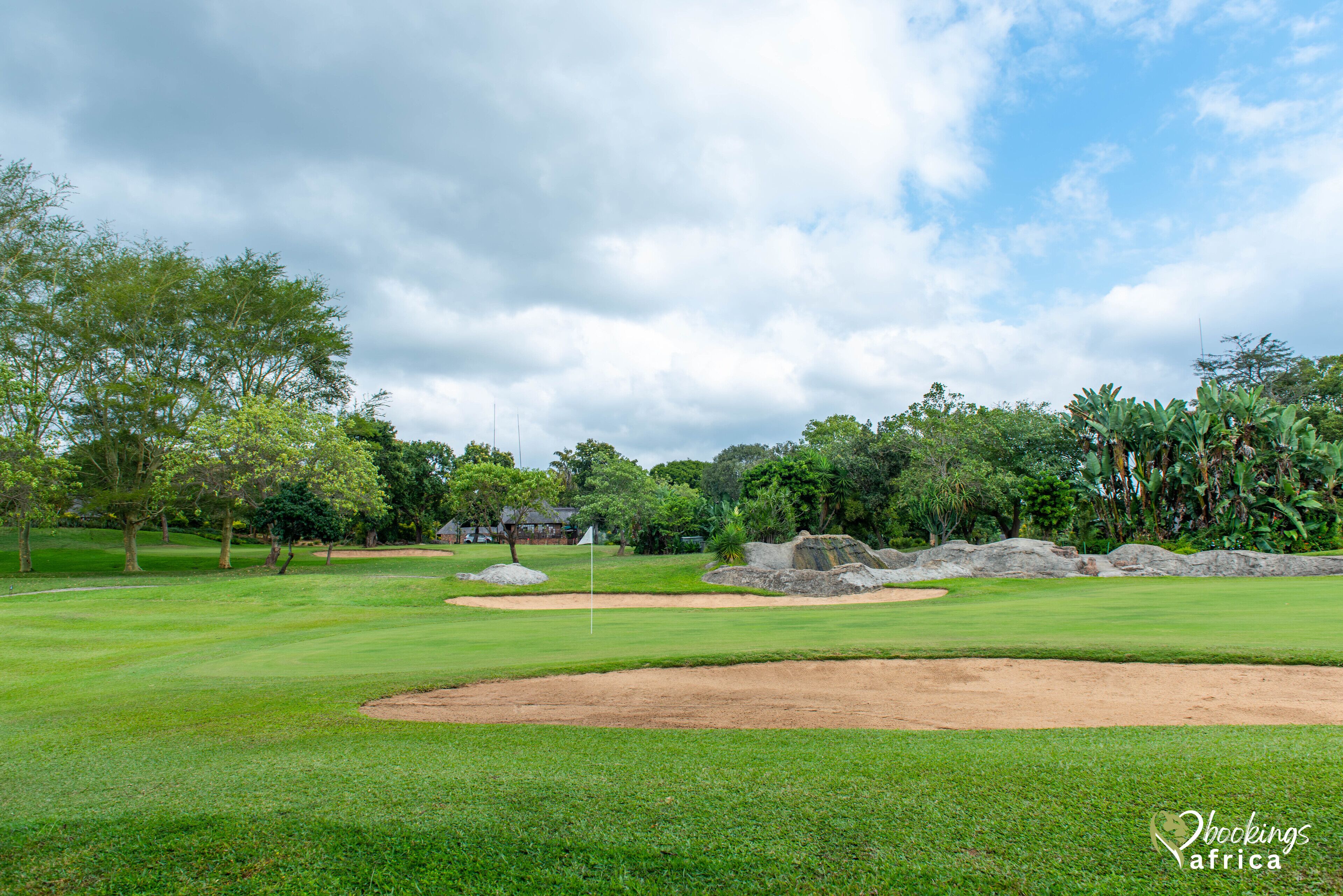 Un campo de golf con búnkeres de arena, una bandera y abundante vegetación.