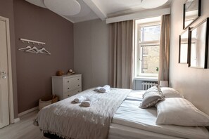 Een slaapkamer met een bed, een dressoir, een raam met gordijnen en een kapstok.