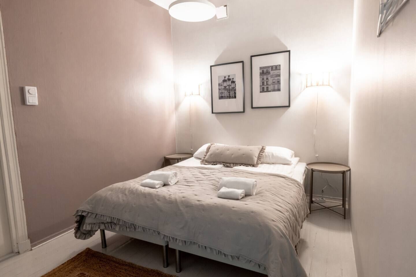 Ein Schlafzimmer mit einem Bett, zwei Nachttischen, einer Wandleuchte und zwei gerahmten Bildern.