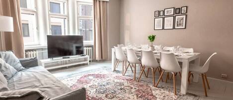 A modern living room with a sofa, TV, dining table with chairs, and a patterned rug.