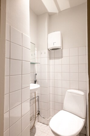A small, white-tiled bathroom with a toilet, a sink, and a shower. - 2ndhomes Bright & Spacious 5BR Apartment (Helsinki)