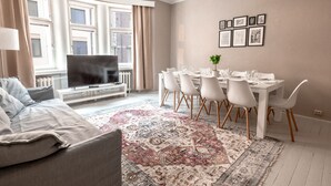 A modern living room with a sofa, a television, a dining table with chairs, and a patterned rug. - 2ndhomes Bright & Spacious 5BR Apartment (Helsinki)
