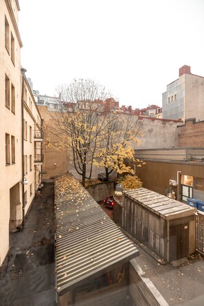 A narrow urban street with buildings on both sides, a tree with yellow leaves, and a metal roof structure. - 2ndhomes Bright & Spacious 5BR Apartment (Helsinki)