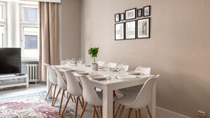 A dining area with a white table set for six, surrounded by white chairs with wooden legs. There is a potted plant on the table, and a radiator is visible to the left. - 2ndhomes Bright & Spacious 5BR Apartment (Helsinki)