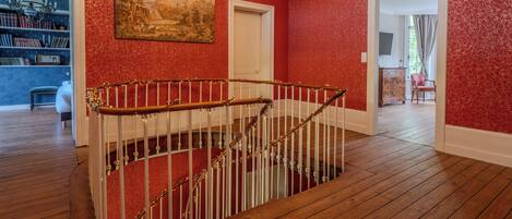 Una escalera con barandilla blanca y escalones de madera, que conduce a una habitación con paredes rojas y un candelabro.