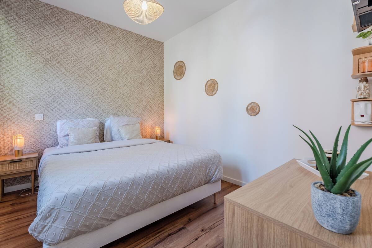 A neatly arranged bedroom with a bed, bedside lamps, a small table with a potted plant, and decorative wall art.