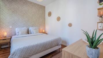 A neatly arranged bedroom with a bed, bedside lamps, a small table with a potted plant, and decorative wall art.