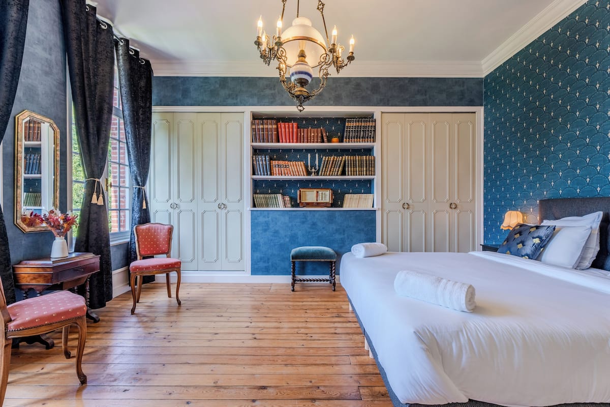 A bedroom with a large bed, a bookshelf, a desk, and a chair.