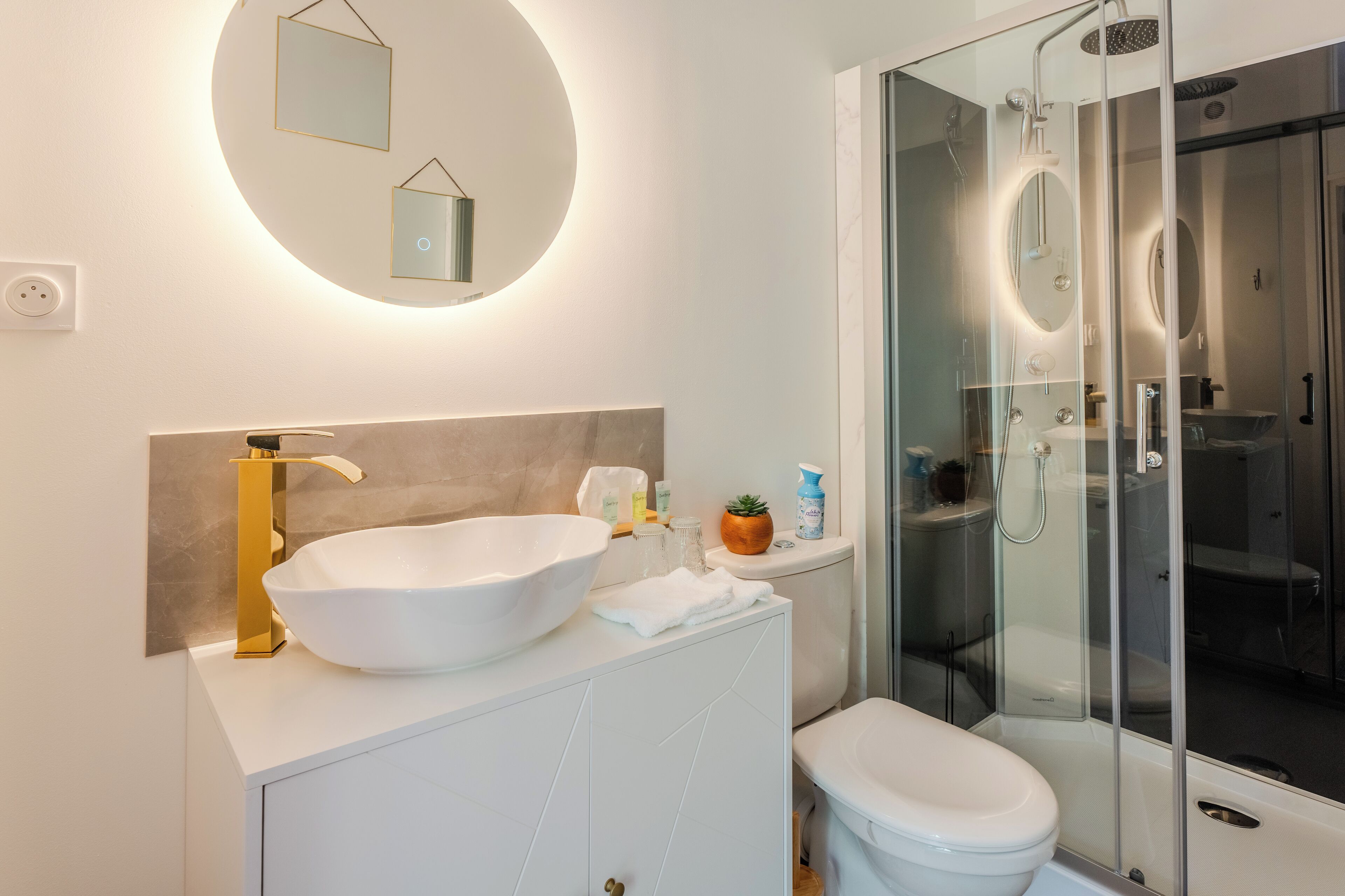 A modern bathroom with a large white sink, gold faucet, and a glass-enclosed shower.