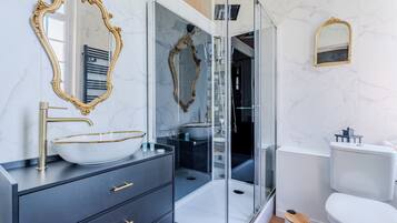 A modern bathroom with a glass-enclosed shower, a white toilet, and a vanity with a gold-framed mirror and a white vessel sink.