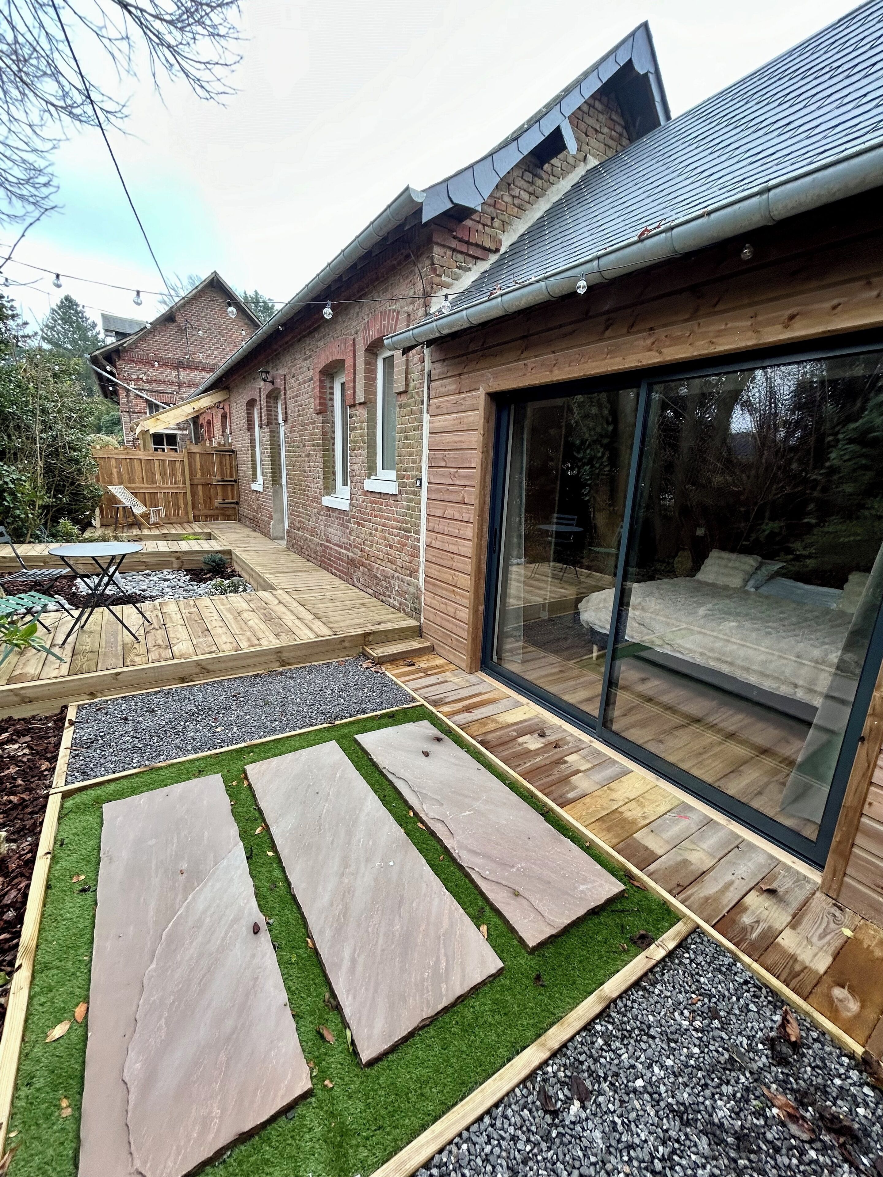 A backyard with a wooden deck, a patio area, and a glass door leading to a covered outdoor space.