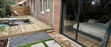 A backyard with a wooden deck, a patio area, and a glass door leading to a covered outdoor space.
