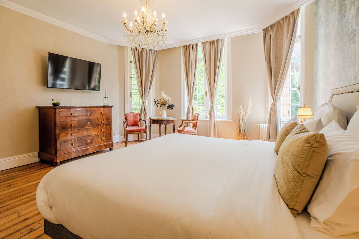 A spacious bedroom with a large bed, wooden dresser, and a television on the wall.