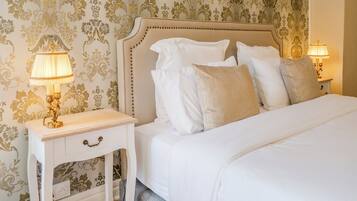 A neatly made bed with white linens and multiple pillows, a bedside table with a lamp, and a wall with ornate wallpaper.