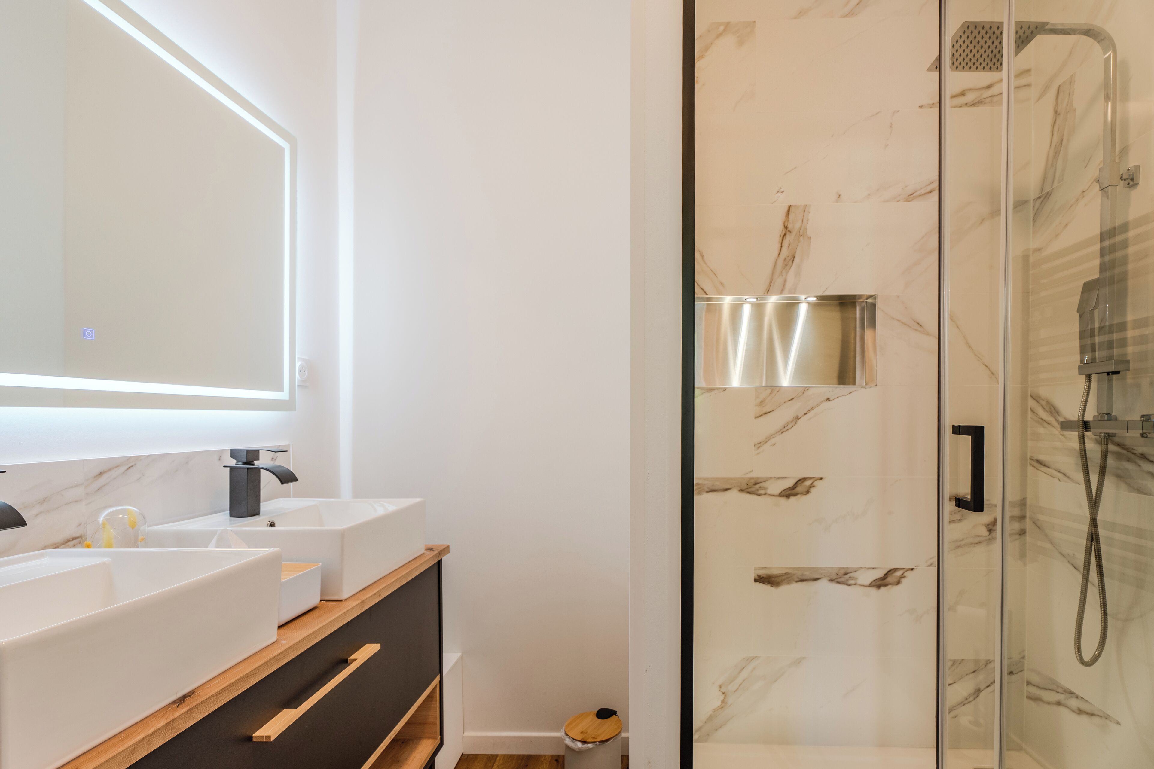 A modern bathroom with a glass-enclosed shower, a large mirror, and a white vanity with multiple sinks.