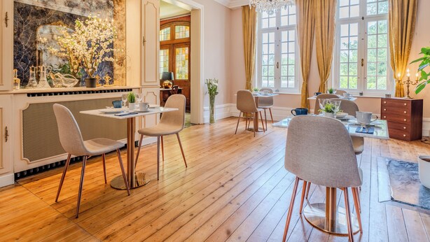 A dining area with wooden flooring, a chandelier, and a large window with curtains. - Le manoir de la belle epoque (Béthencourt-sur-Mer)